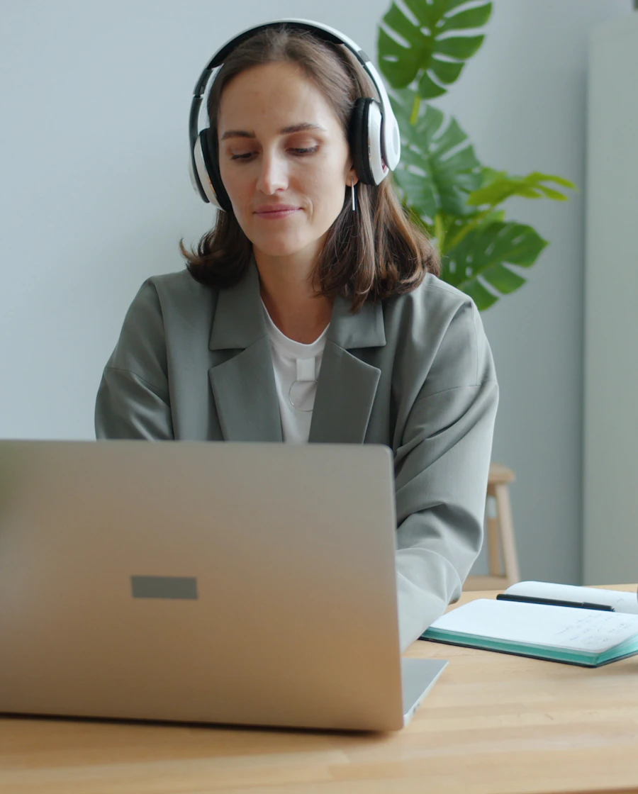 Assistant wearing headphones working on a laptop at a bright desk